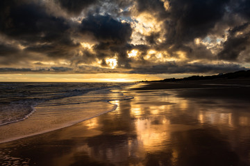 Storm clouds dyed golden colors during sunset at the beach