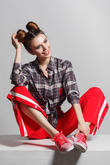 A picture of a fun, positive model wearing a plaid shirt, red sweatpants and sneakers. Studio photo session