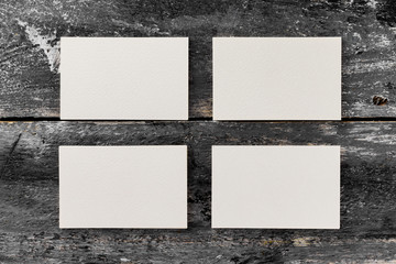 Mockup of four white horizontal blank business cards at wooden vintage table background.