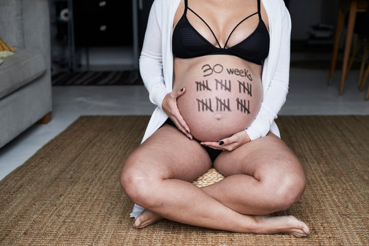 Close-up of pregnant woman sitting on the floor at home with tally marks on her belly