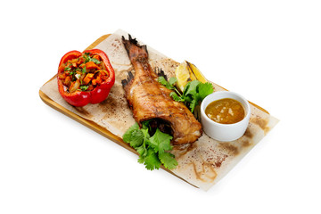 Grilled fish with no head served on paper at wooden board with parsley, pepper, lemon and sauce isolated at white background.