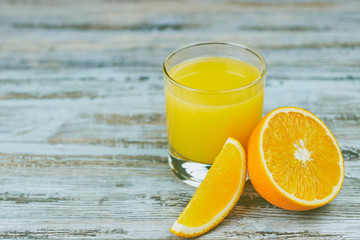 a glass of fresh orange juice with fresh citrus fruits on a light wooden table. horizontal view. citrus juice