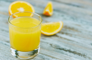 a glass of fresh orange juice with fresh citrus fruits on a light wooden table. horizontal view. citrus juice