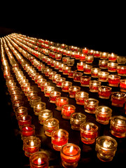 Opferlichter brennen in der Kirche - viele rote Kerzen auf schwarzem Hintergrund