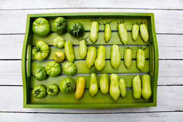 Wooden tray with various tomatoes, stage of ripeness, unripe