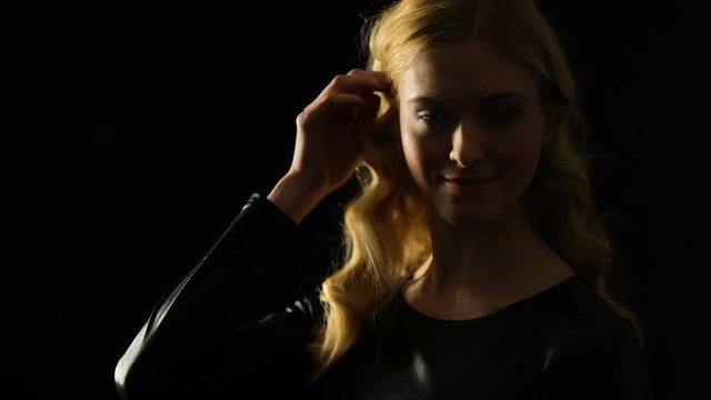 Blond woman flirting and playing with hair against black background, seduction