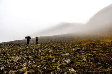 two Hikers climbing the stony steep hill, clouds hang on the mountains, Fall in Spitzbergen,...