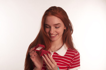 The portrait of an young redhead lady with a gift box in her hands isolated over white background posing