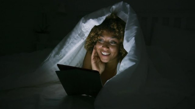 Woman using tablet under blanket