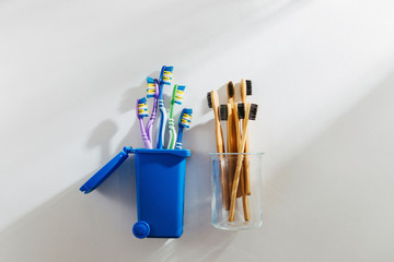 Eco friendly bamboo toothbrushes in glass and plastic toothbrushes in trash bin. Zero waste, plastic free, ecology concept.