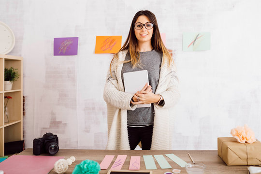 Portrait of smiling young woman standing at desk with handmade things