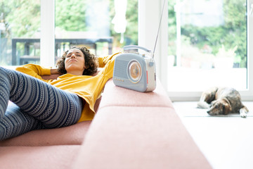 Woman lying on couch listening to music with portable radio at home