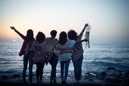 Romantic and dreamer concept image with five friends women hug each other viewed from back looking at the sunset holiding light - love freedom and wanderlust for group of people