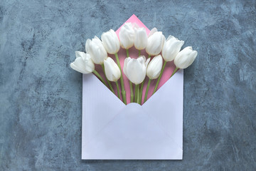 Springtime flat lay, white tulips in white and pink envelope on grey background, copy-space