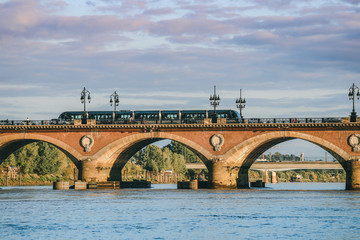 Obraz premium View of Tram is crossing Pont de Pierre bridge or Pont de Pierre in the morning from Garonne river, Bordeaux, France