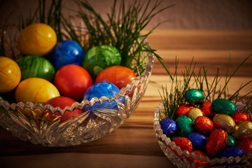 Bunter Ostereier in einer Kristallschüssel mit grünem Gras und Holz Hintergrund und dunkler Vignette.