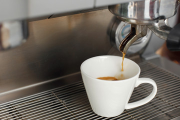 Close-up of freshly brewed coffee is poured from a coffee machine into a white cup