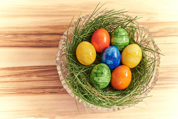 Ostereier in einer Kristallschüssel in grünem Gras mit einem Hintergrund aus Nussbaum und heller Vignette.