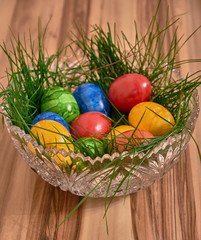 Ostereier in einer Kristallschüssel in grünem Gras mit einem Hintergrund aus Nussbaum.