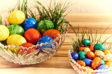 Bunte Ostereier in einer Kristall Schüssel mit grünem Gras, Holz Hintergrund. und heller Vignette.