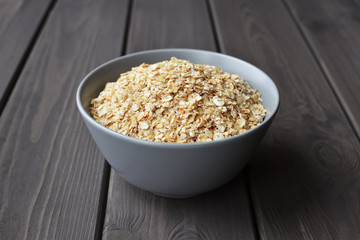 Rolled oats in ceramic bowl on dark wooden table with texture