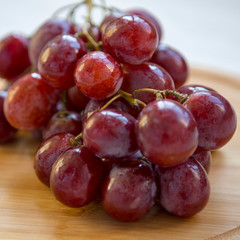 Bunch of ripe red grape on a round bamboo board, side view. Close-up.