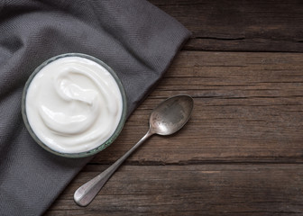 Fototapeta na wymiar White yogurt in glass bowl on old wooden desk with spoon on right side.