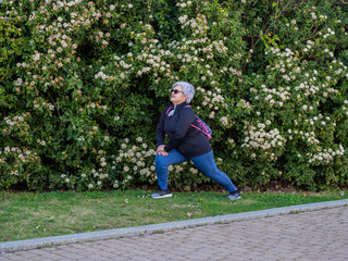 Fototapeta premium A senior woman with white hair practicing gymnastics in an urban park