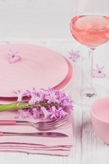 Pink rustic table setting with purple hyacinth flowers, linen napkin and glass of rose wine on white wooden table