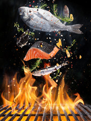 Tasty fishes flying above cast iron grate with fire flames. Freeze motion barbecue concept.