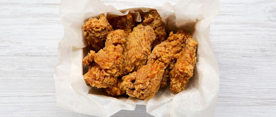 Chicken wings in paper box on a white wooden background, overhead view. Flat lay, top view. Close-up.