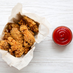 Tasty fried chicken wings in paper box with ketchup over white wooden surface, view from above. Top view, from above, overhead.