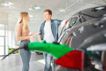 Young couple buying a first electric car in a showroom. Ecological vehicle concept. Modern...