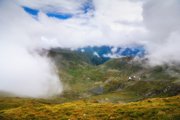 Amazing landscape of summer mountains. View of fog and low clouds over Fagaras Mountains are the highest mountains of the Southern Carpathians. Transylvania. Romania. Travel background. 