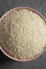 Dry white rice basmati in a pink bowl over gray surface, top view. Flat lay, overhead, from above. Close-up.