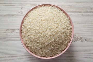 Dry white rice basmati in a pink bowl over white wooden background, top view. Flat lay, overhead, from above.