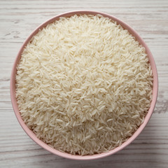 Dry white rice basmati in a pink bowl over white wooden surface, top view. Flat lay, overhead, from above.