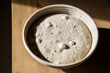 Sourdough bread proofing in a basket with visible gas bubbles. Homemade baking.