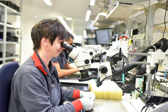 Woman using a microscope for the quality control in the manufacturing of circuit boards for the electronics industry