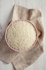 Dry white rice basmati in a pink bowl over white wooden background, top view. Flat lay, overhead, from above.