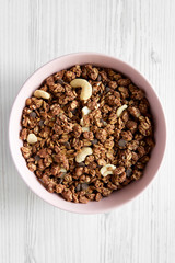 Homemade chocolate granola with nuts in a pink bowl over white wooden background, top view. From above, overhead.