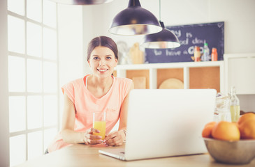 Young woman in kitchen with laptop computer looking recipes, smiling. Food blogger concept.