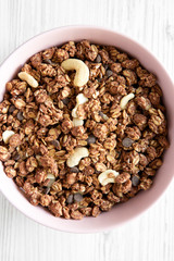 Homemade chocolate granola with nuts in a pink bowl over white wooden surface, top view. From above, overhead. Close-up.