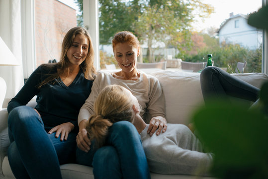 Happy mother with two teenage girls on couch at home