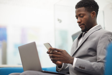 Side view portrait of handsome African businessman using smartphone while working in office, copy space