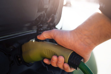 Electric vehicle charging station. Close-up of hand charging an electric car with the power cable supply plugged in. Eco-friendly car for environment