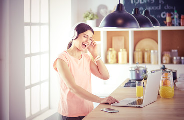Young woman in kitchen with laptop computer looking recipes, smiling. Food blogger concept.