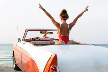 Sexy woman wearing  red swimsuit  is sitting inside a retro cabriolet car