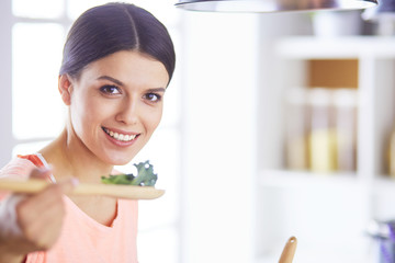 Smiling young woman mixing fresh salad in the kitchen.