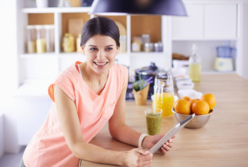 Beautiful young woman using a digital tablet in the kitchen.